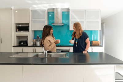 two people in a kitchen talking with coffee mugs