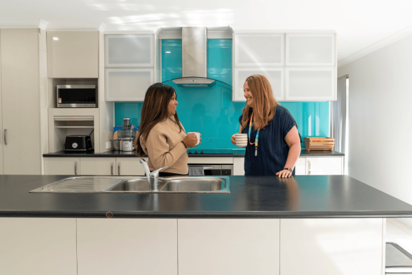 two people in a kitchen talking with coffee mugs