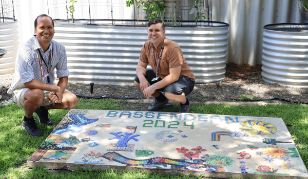 two people crouched next to a mosaic artwork smiling