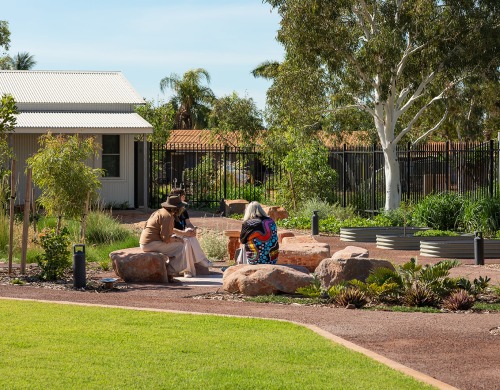 3 people sitting outside on rocks in a yarning circle surrounded by a garden