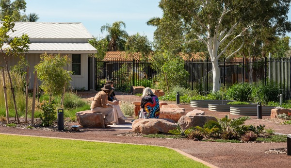 3 people sitting outside on rocks in a yarning circle surrounded by a garden