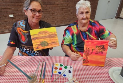 Two women showing pieces of artwork that they have each painted