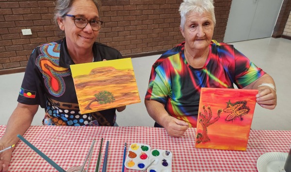 Two women showing pieces of artwork that they have each painted
