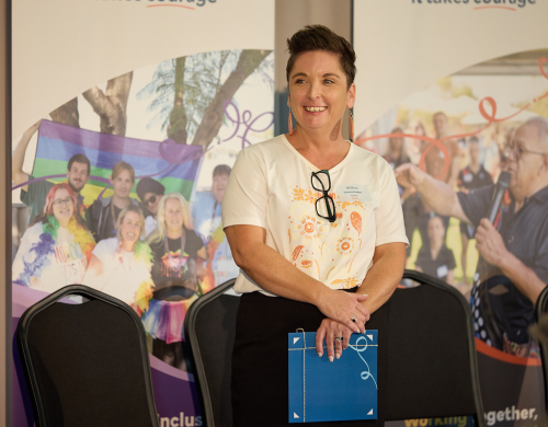 woman standing on stage smiling holding an award folder